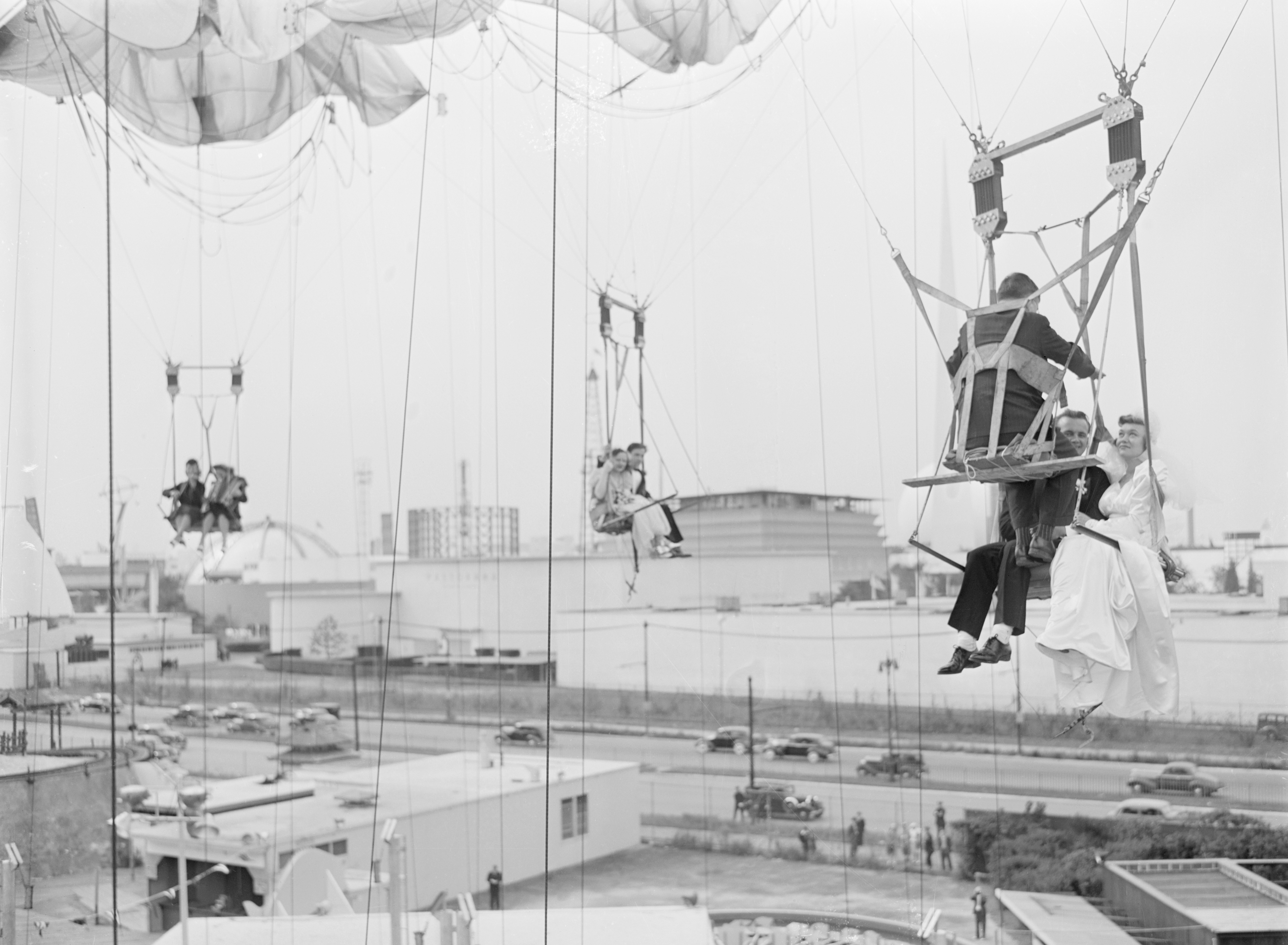 People riding chair swings suspended high in the air at an amusement park, with a cityscape in the background