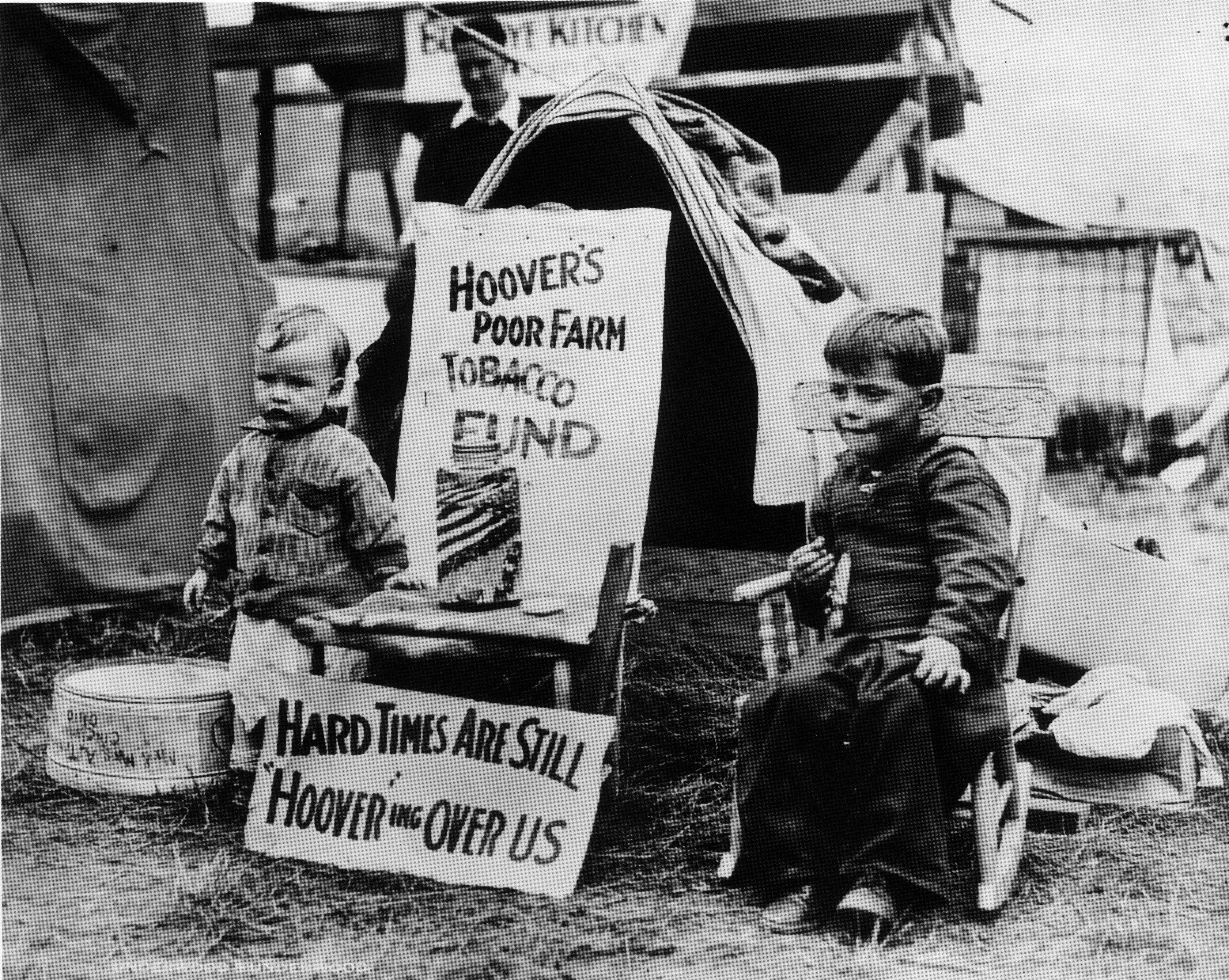 Two children sit with a sign about poor farm conditions during the Great Depression, highlighting economic struggles and referencing Hoover's policies