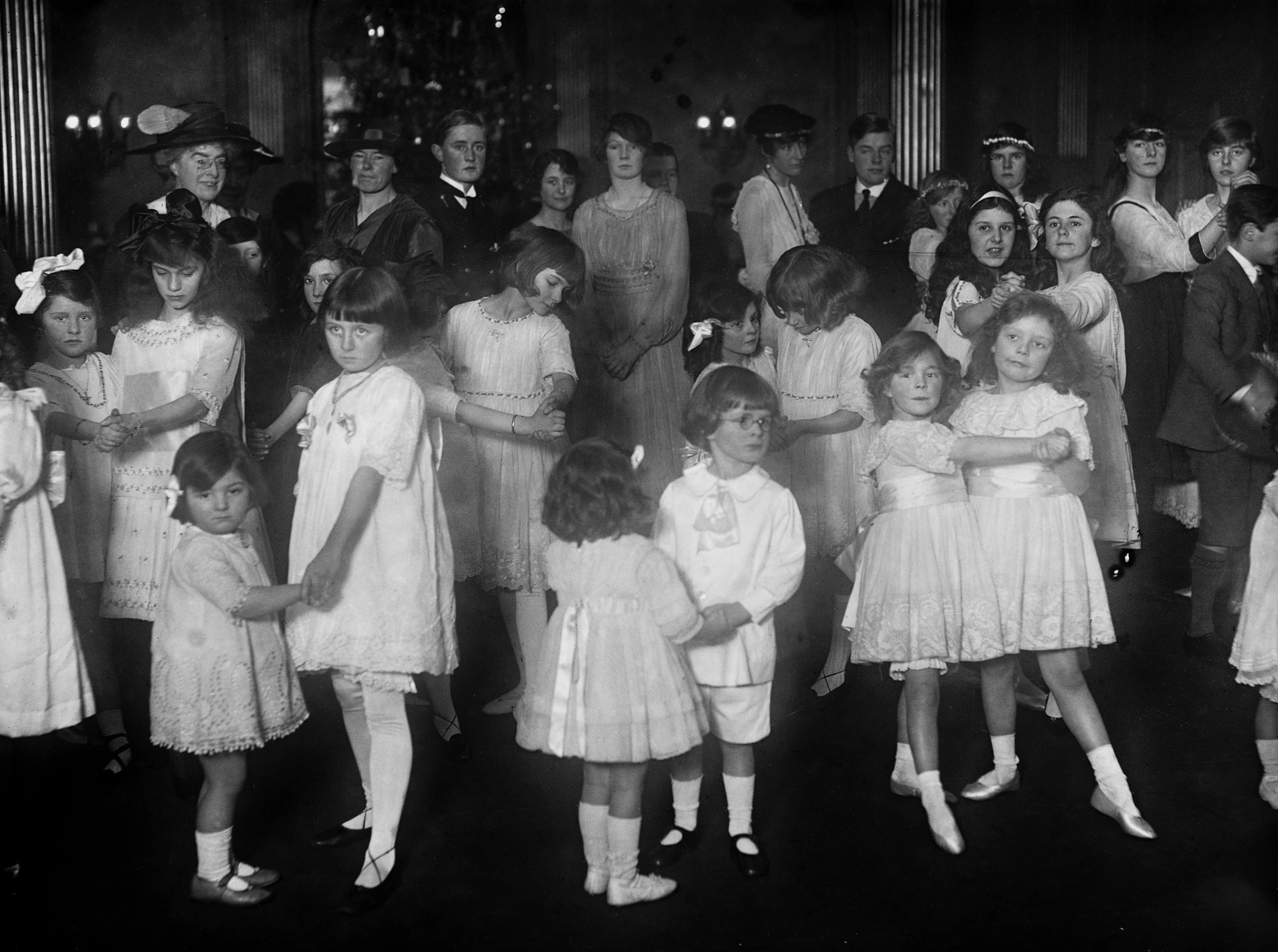 Children in formal attire attend a social gathering, engaging in conversation and activities in a crowded space
