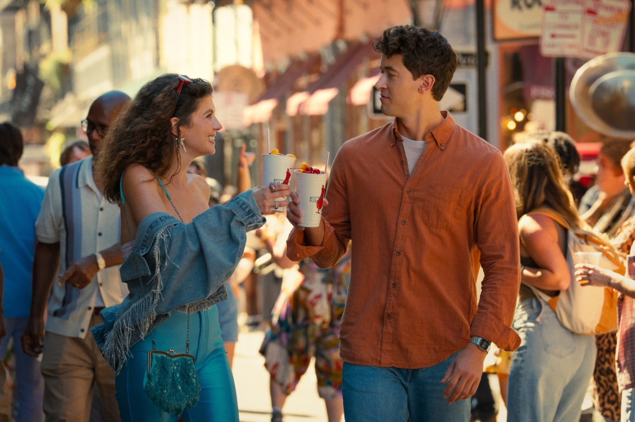 Emily Bader and Tom Blyth walking outdoors, smiling and toasting with drinks in New Orleans