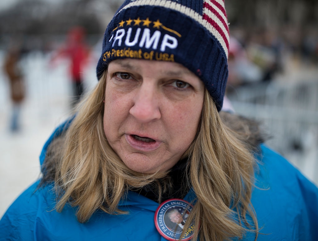Person wearing a Trump beanie and a coat, outdoors, with a badge featuring an image