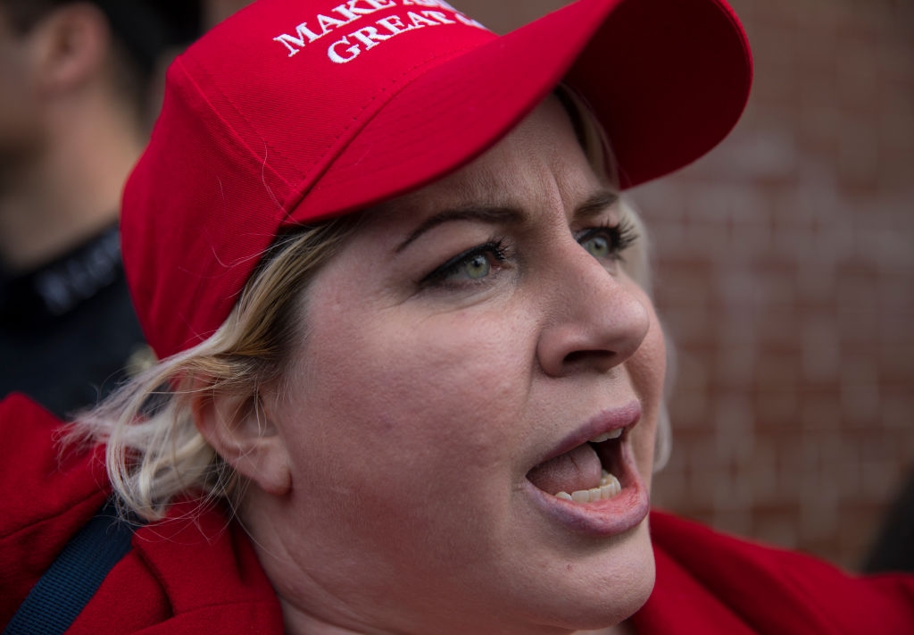 Person in a red baseball cap and jacket, appearing to speak passionately. The hat features text