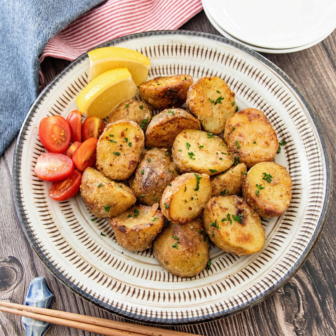 お皿に盛られた焼きポテト、スライスされたレモンとチェリートマト。テーブルセッティングと箸が添えられている。
