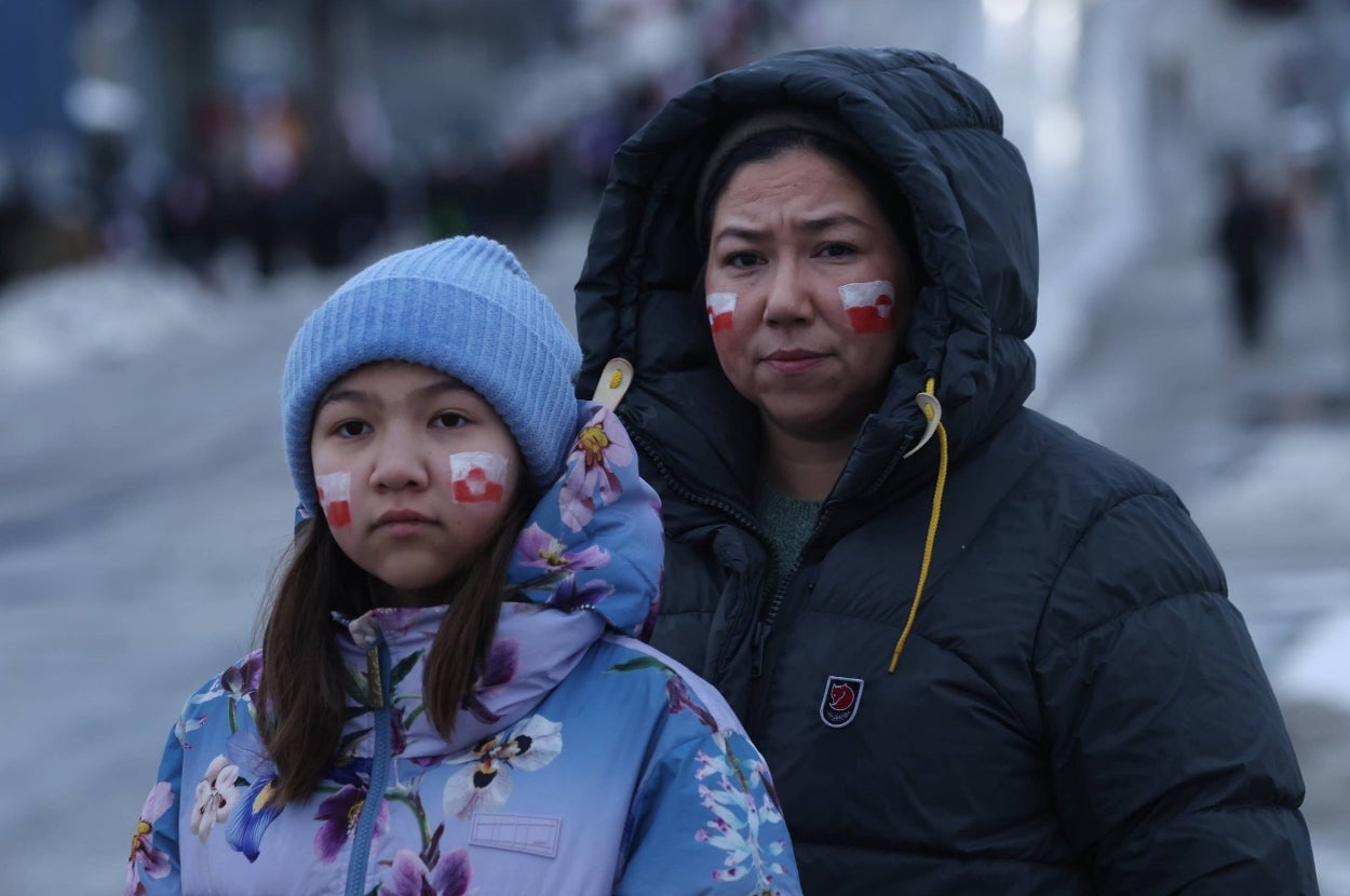 Two people outdoors wearing winter jackets. They have face paint with red and white patterns, standing on a snowy street