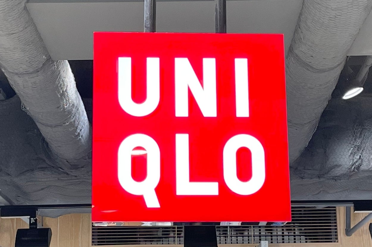 Uniqlo store interior with a red and white logo sign hanging from the ceiling, shelves displaying folded clothing beneath