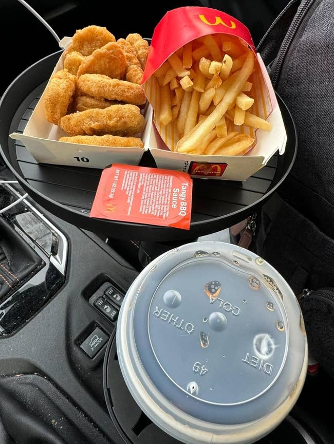 Fast nutrient  repast  with chickenhearted  nuggets, fries, a soda, and barbecue condiment  successful  a car's interior