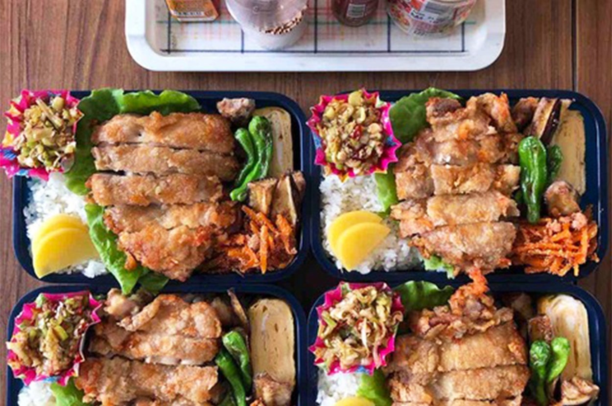 4つの唐揚げ弁当が整然と並べられている。レモンスライス、野菜、ライスが付いている。背景に調味料類が見える。