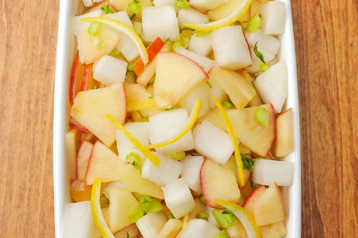 白い皿に盛られたダイコン、リンゴ、レモンのスライスと緑のトッピングが見えるサラダ。