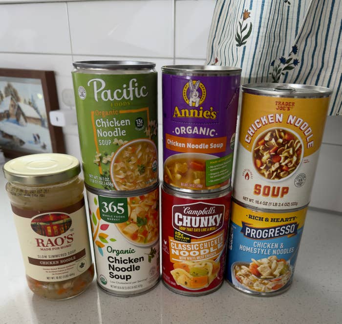Various brands of chicken noodle soup cans and a jar are displayed on a counter
