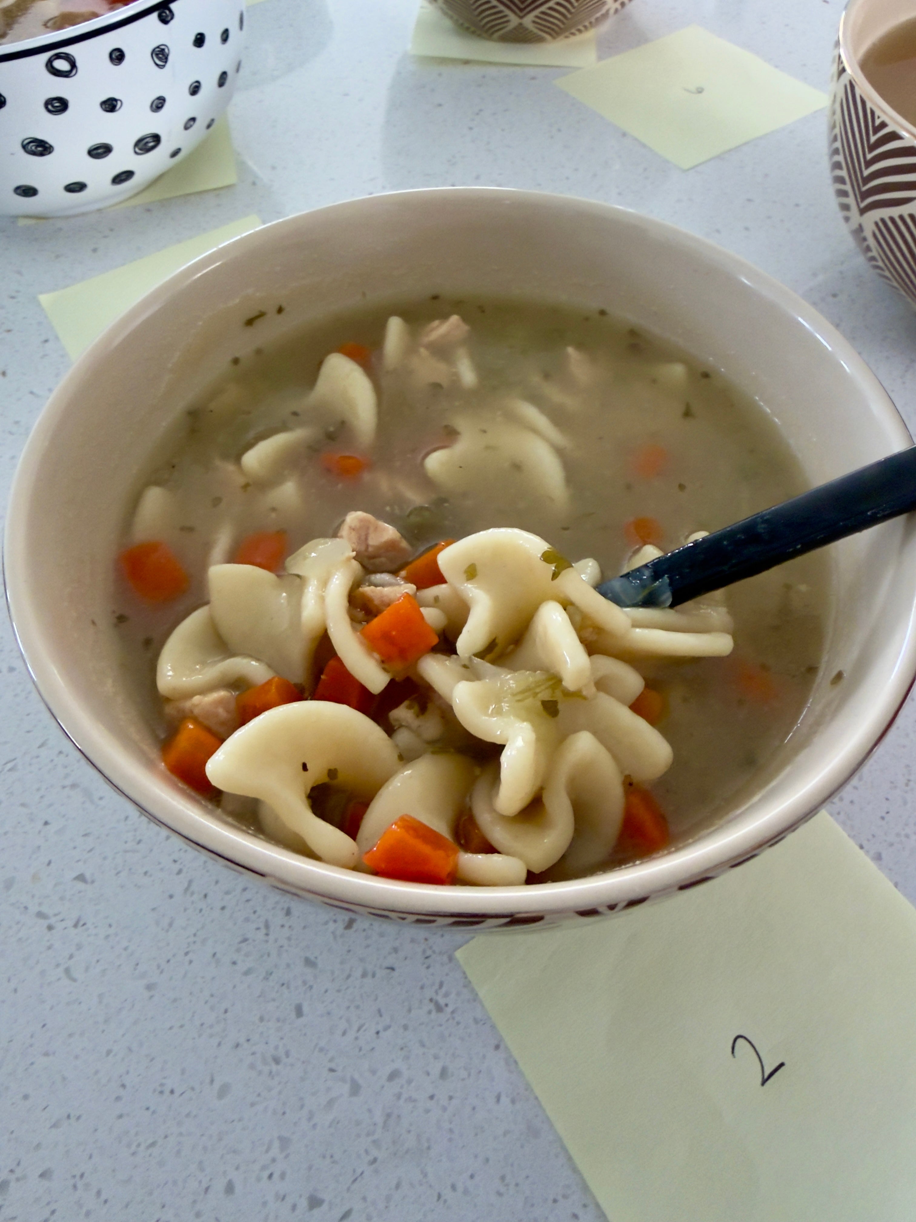 Bowl of chicken noodle soup with vegetables and a spoon on a table
