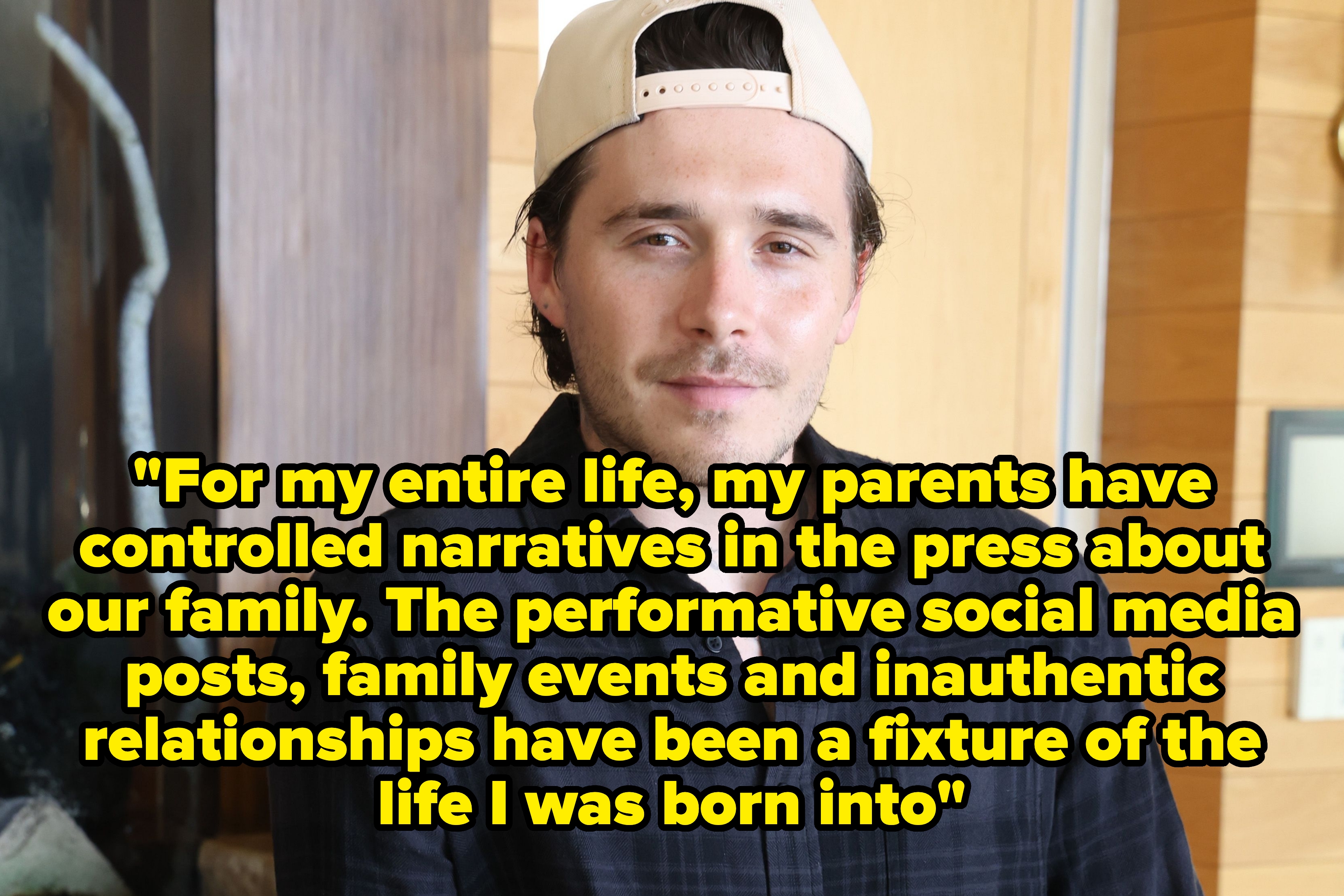 A man in a casual plaid shirt and a backwards cap leans against a countertop with a cocktail nearby