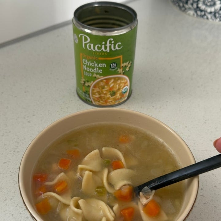 Bowl of chicken noodle soup with vegetables and a can of Pacific chicken noodle soup in the background on a kitchen counter