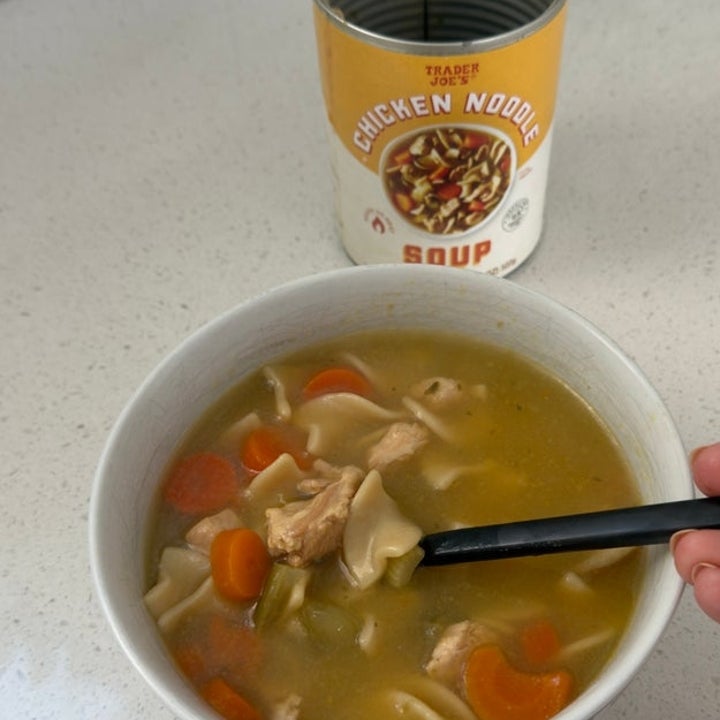 A bowl of chicken noodle soup with vegetables and chunks of chicken, next to an opened can of store-bought soup