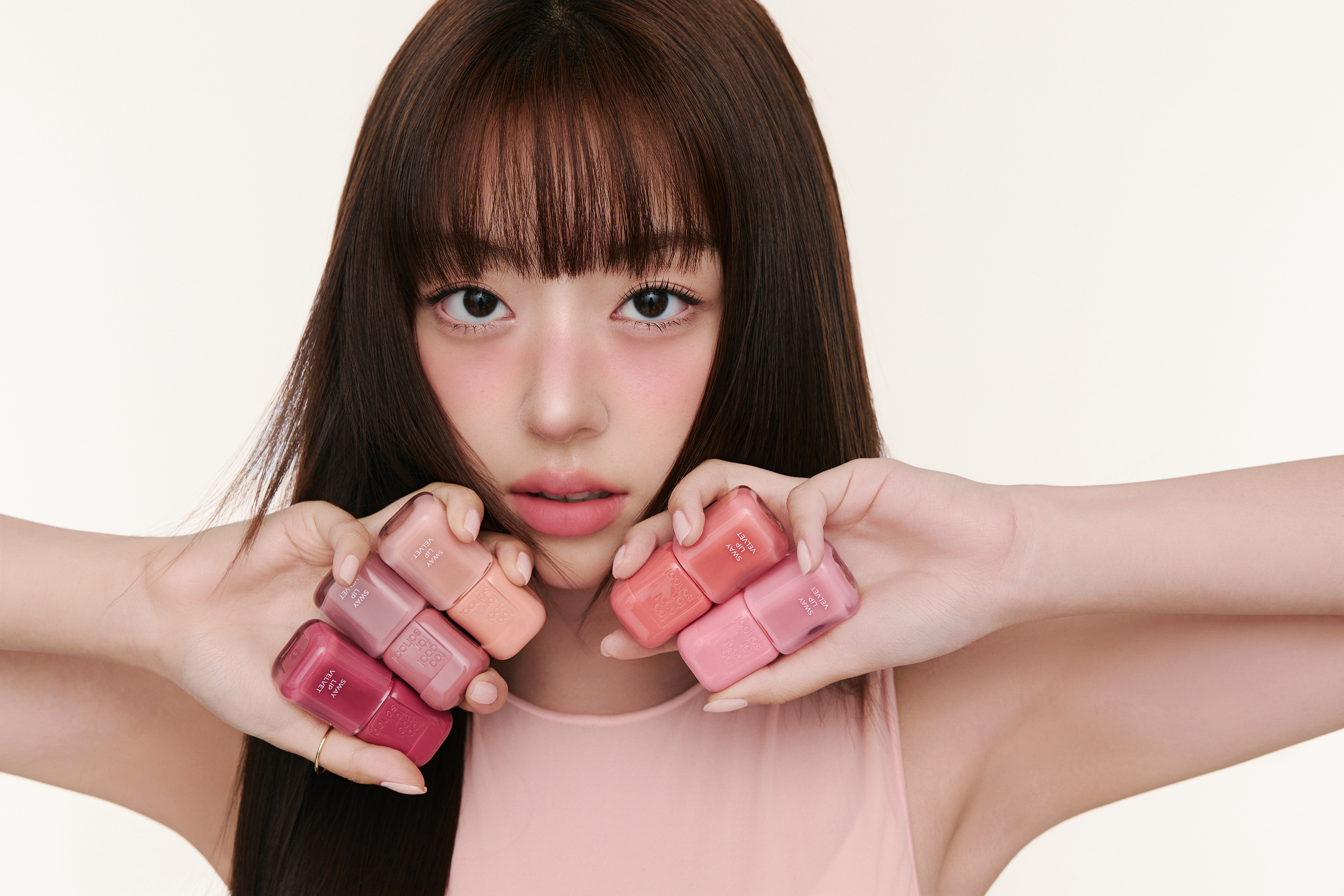 女性がピンク系の爪にカラーを持ちながら、指を顔の前に広げている。