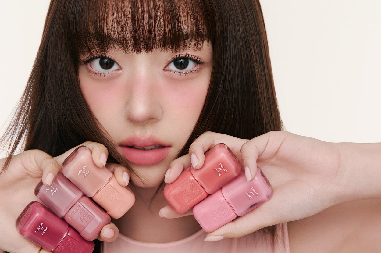 女性がピンク系の爪にカラーを持ちながら、指を顔の前に広げている。