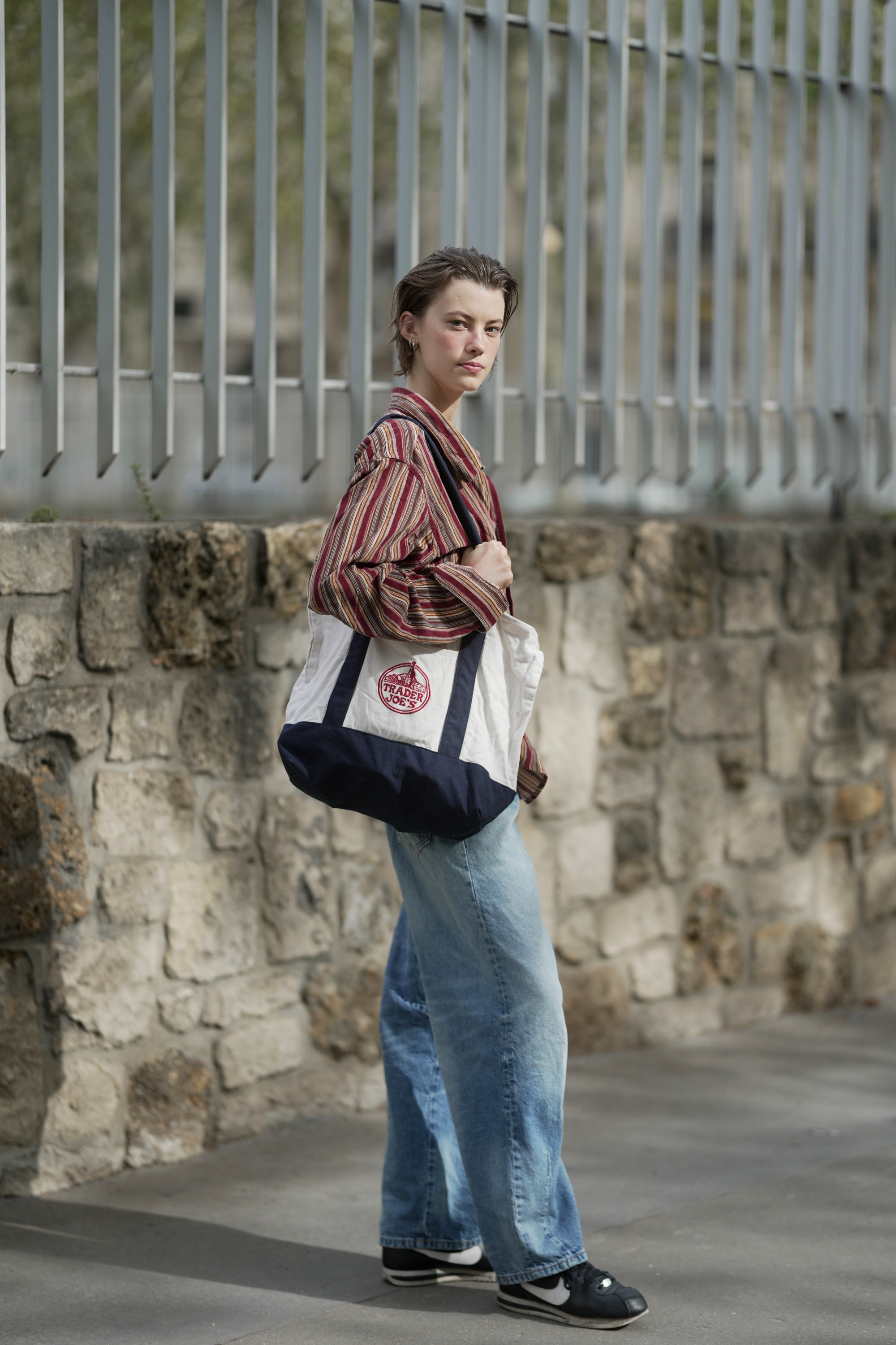 Woman wearing a striped jacket, jeans, and carrying a large Trader Joe's canvas tote bag