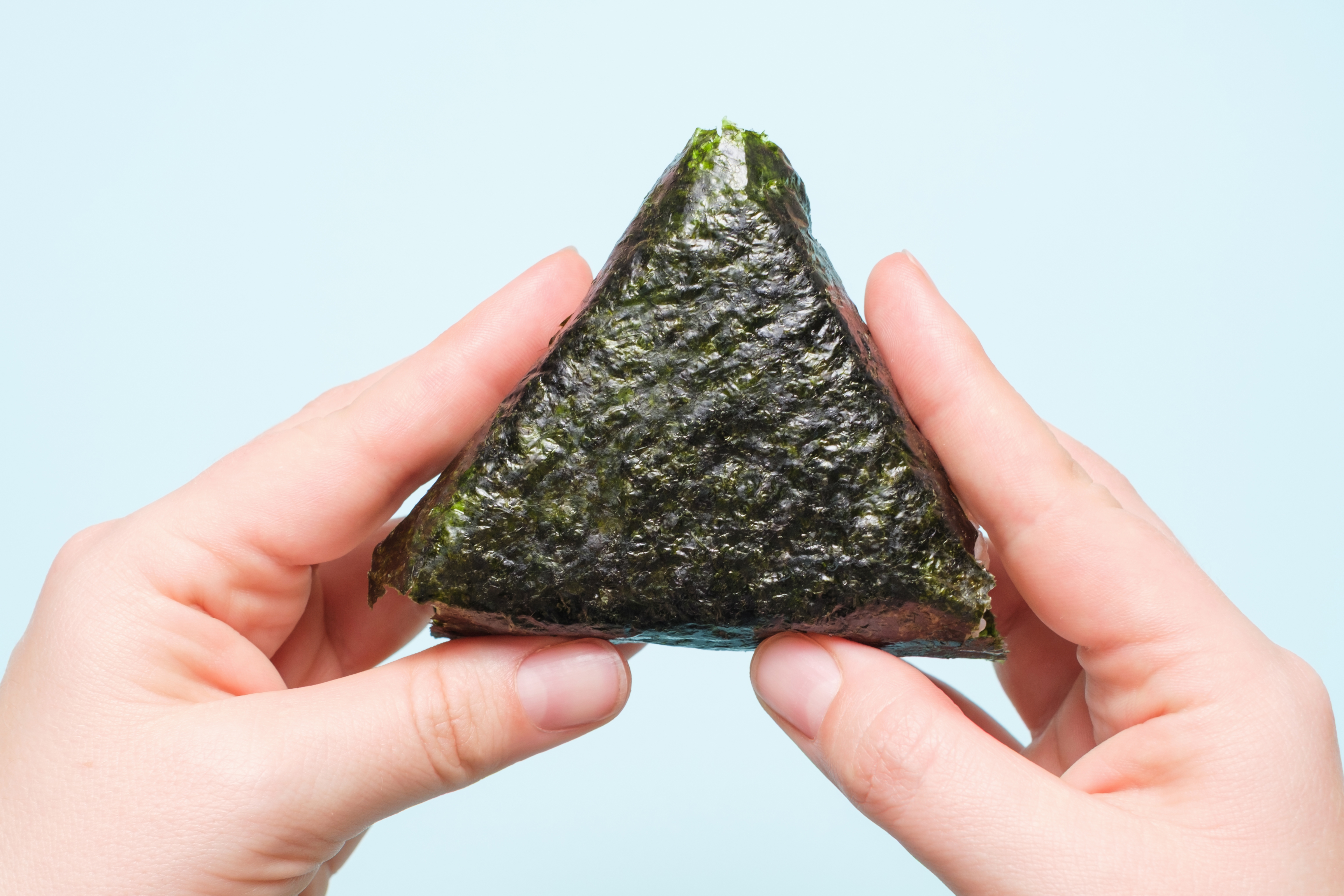 Hands holding a triangular kimbap wrapped in seaweed