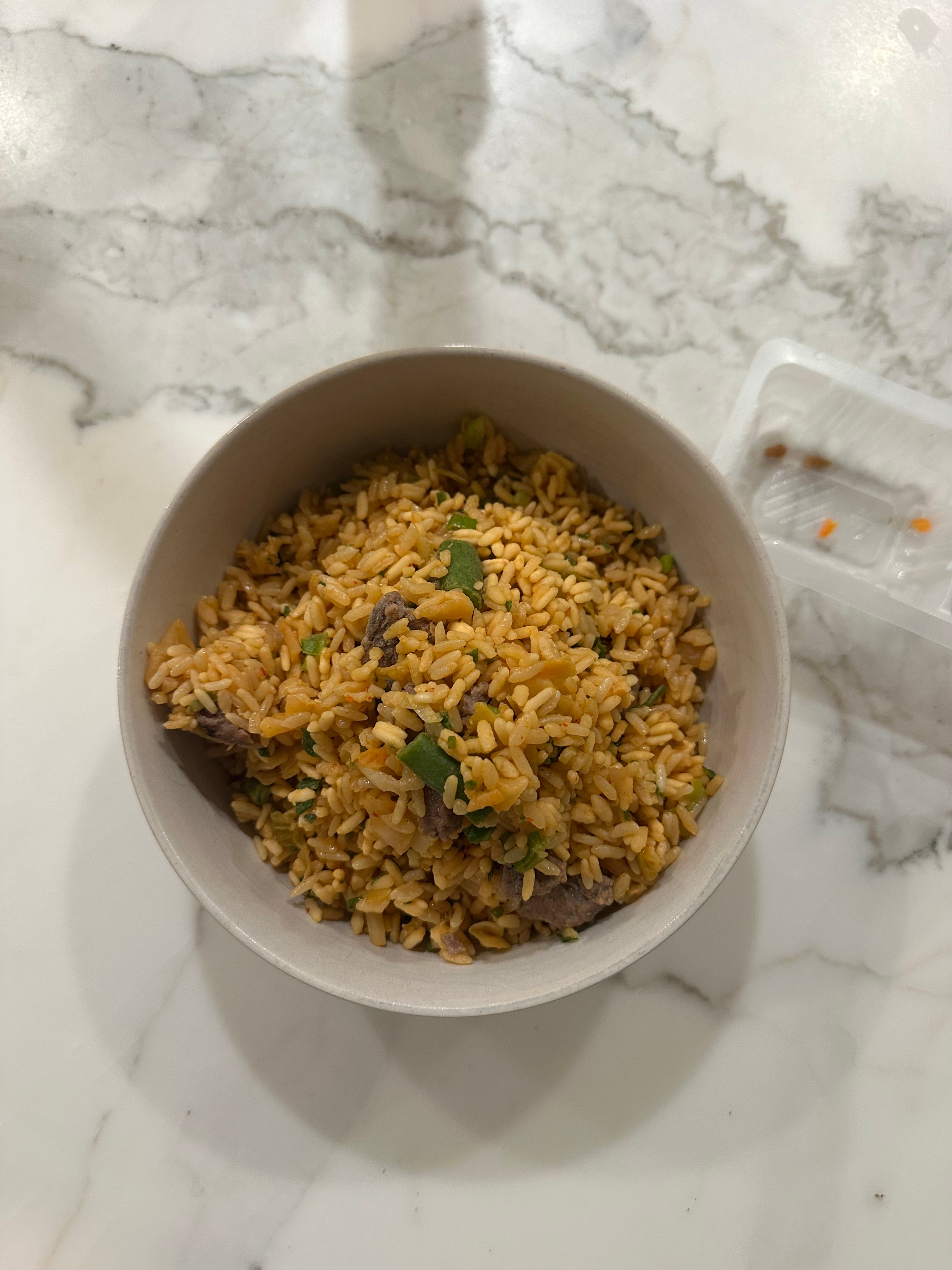 A bowl of seasoned rice mixed with herbs and bits of meat, placed on a marble countertop