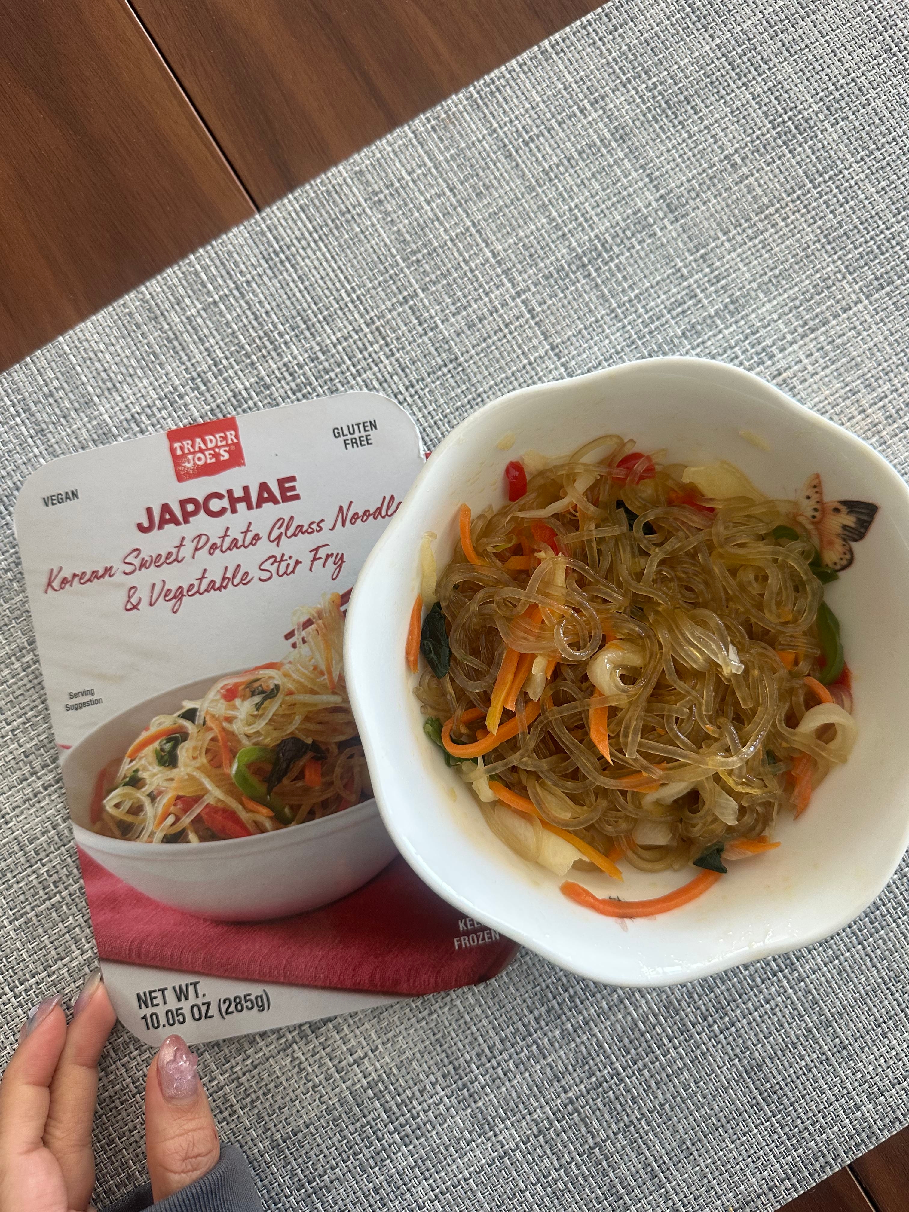 Bowl of Japchae glass noodles with vegetables beside its Trader Joe's packaging on a table