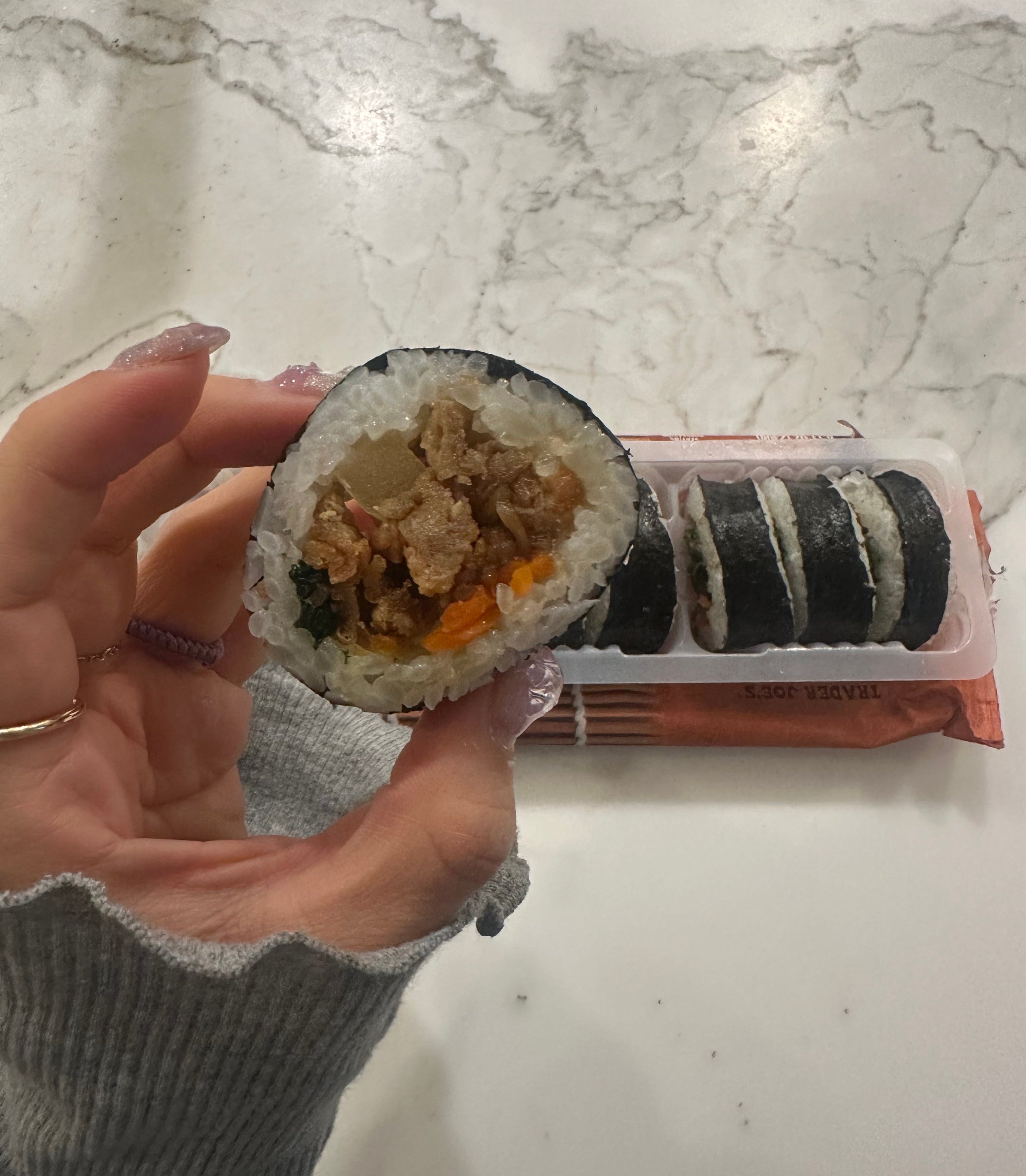 Hand holding a piece of kimbap with the remaining pieces on a tray in the background