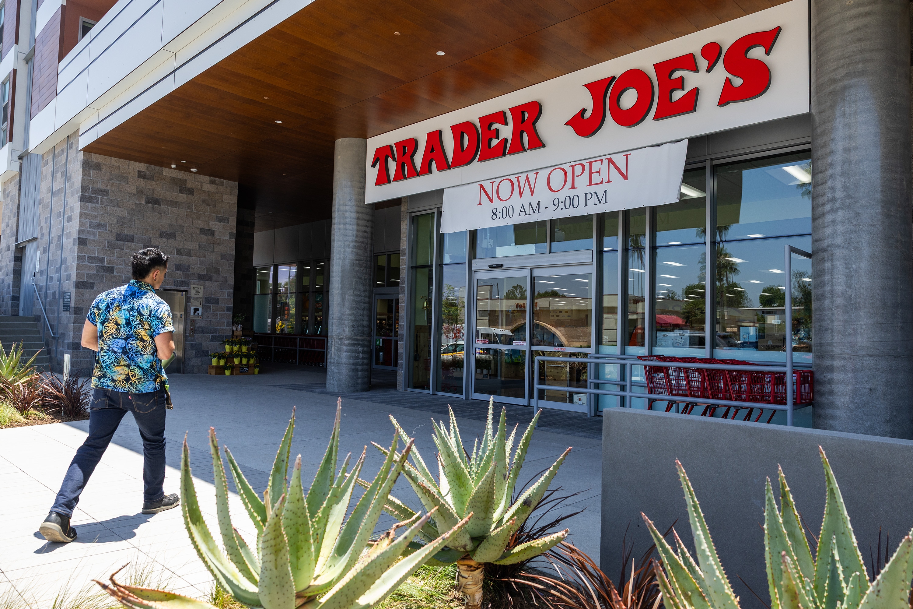 A Trader Joe's employee in a floral shirt walks toward the store entrance