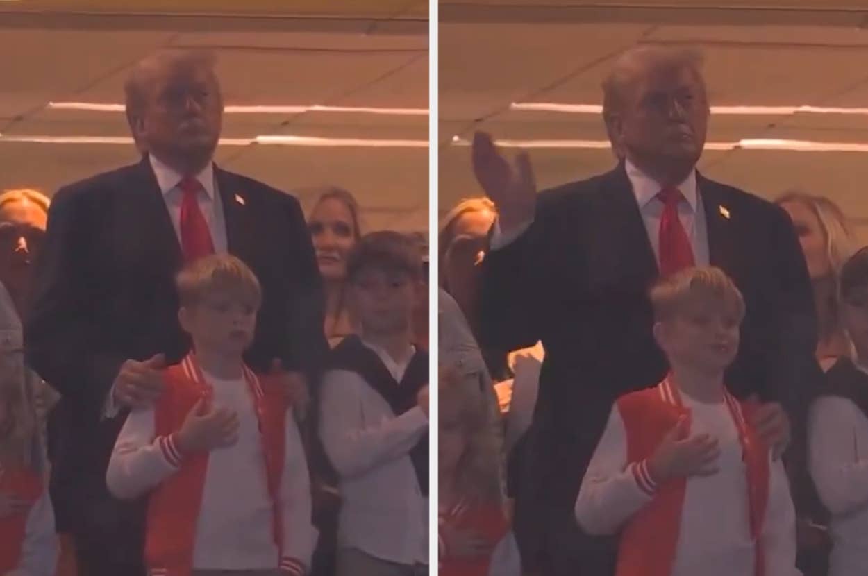 A man in a suit stands with others, one hand on a child's shoulder, during a public event