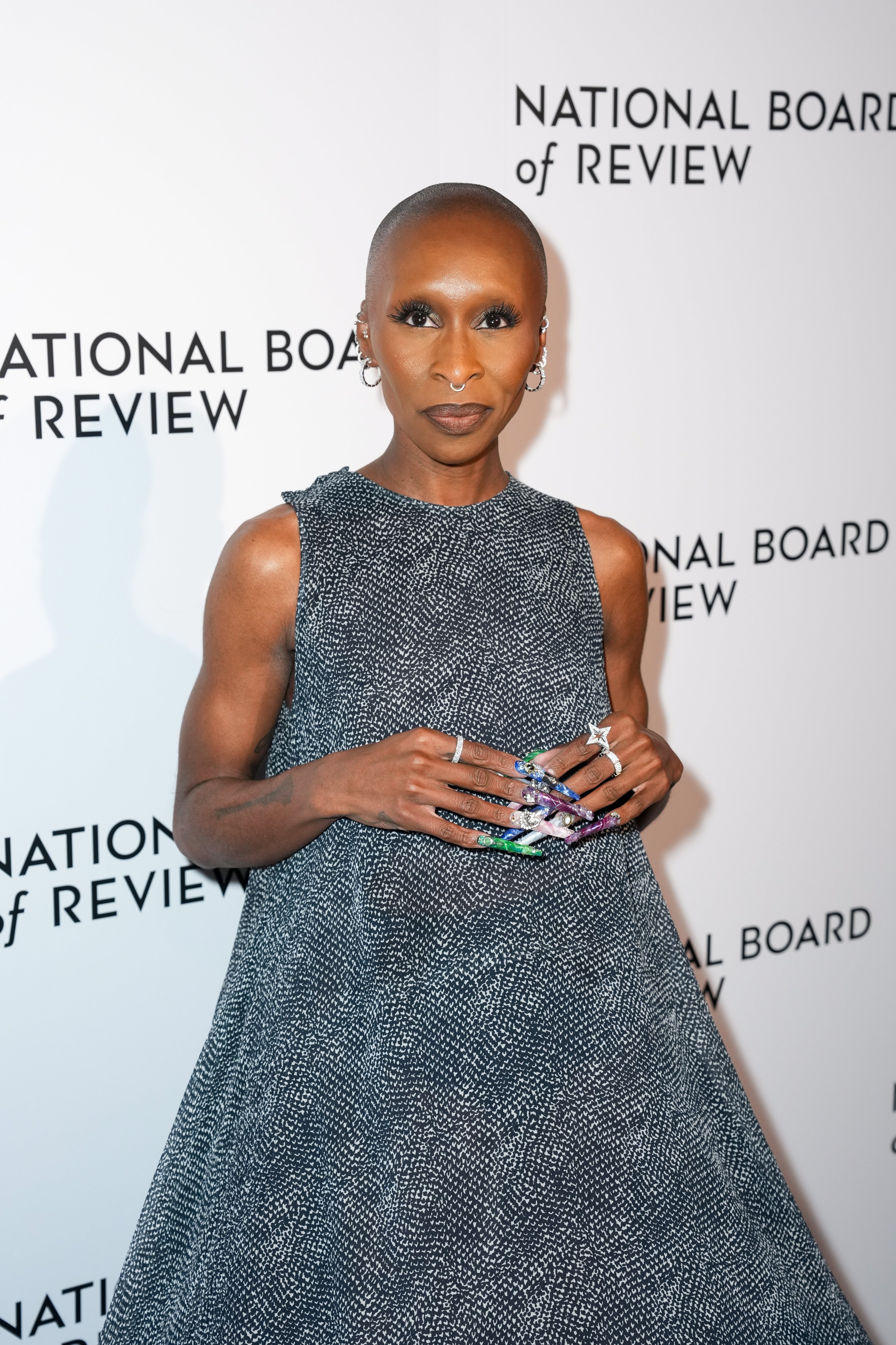 Person successful  textured, sleeveless formal  poses astatine  National Board of Review lawsuit   backdrop, showcasing elegant jewelry and manicured nails