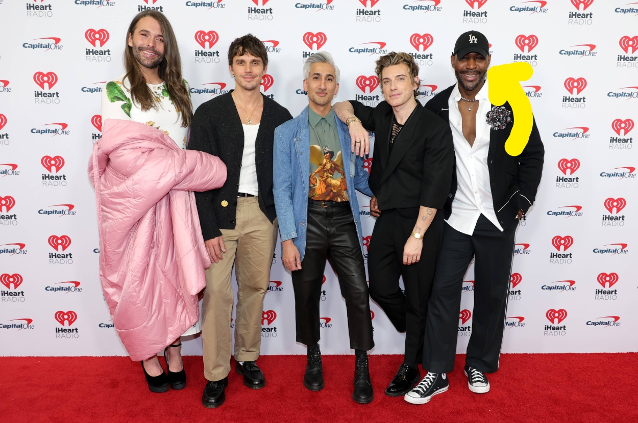 Group of five people posing on a red carpet event. Outfits vary from casual to trendy, with one person holding a pink coat and another in a black jacket with a hat