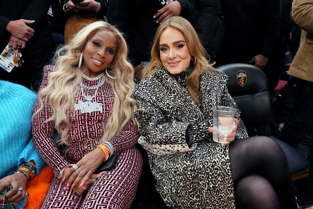 Two women seated astatine  an event; 1  is successful  a patterned jumpsuit, the different   successful  a leopard people     coat, some  smiling astatine  the camera