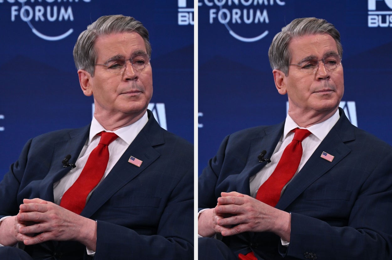 A man in a suit, wearing a red tie and an American flag pin, sits attentively at an economic forum panel discussion