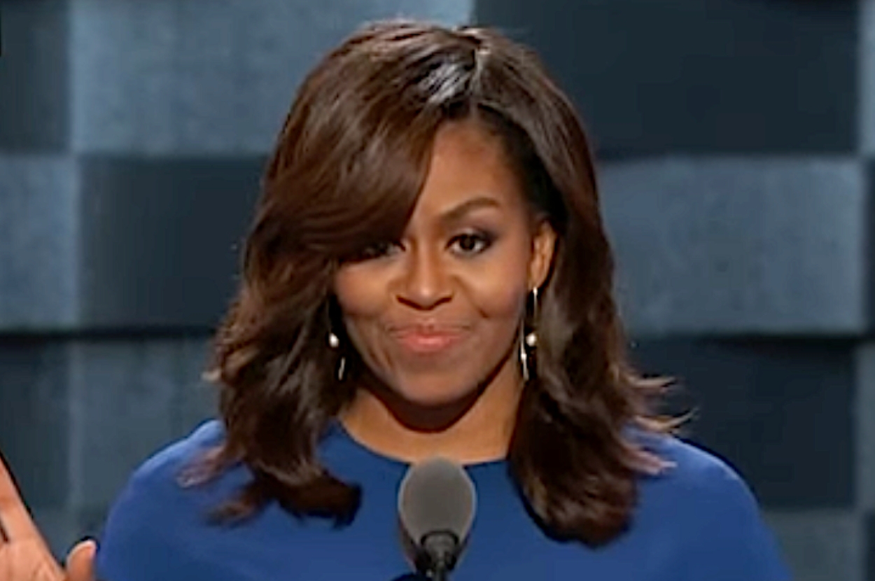 A person in a blue outfit speaks at a podium with a microphone, appearing confident and poised
