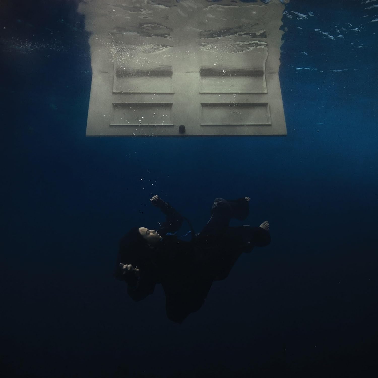 Person submerged underwater beneath   a floating door, creating a surreal scene