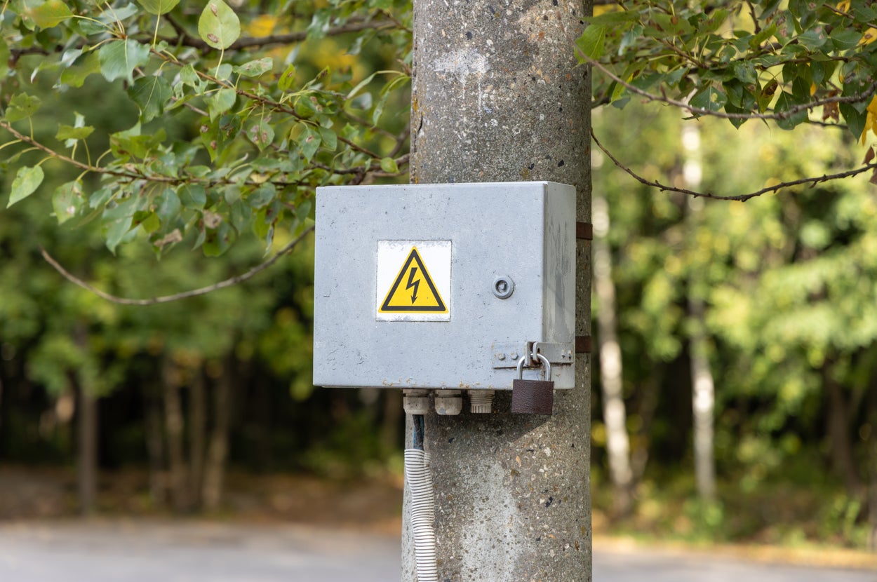 電柱に設置された電気警告標識付きの制御ボックス。背景は森。
