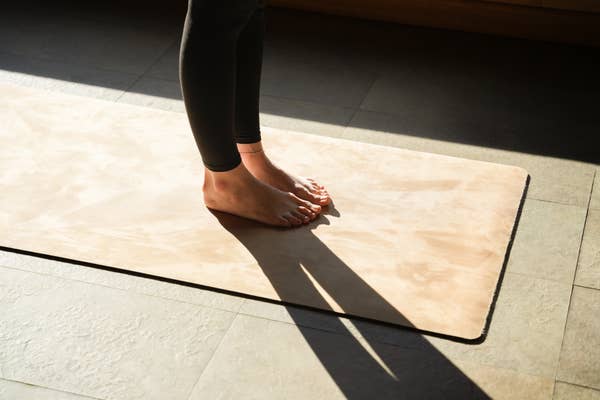 Person standing on yoga mat in a sunlit room, feet planted and shadows long, suggesting morning or evening practice