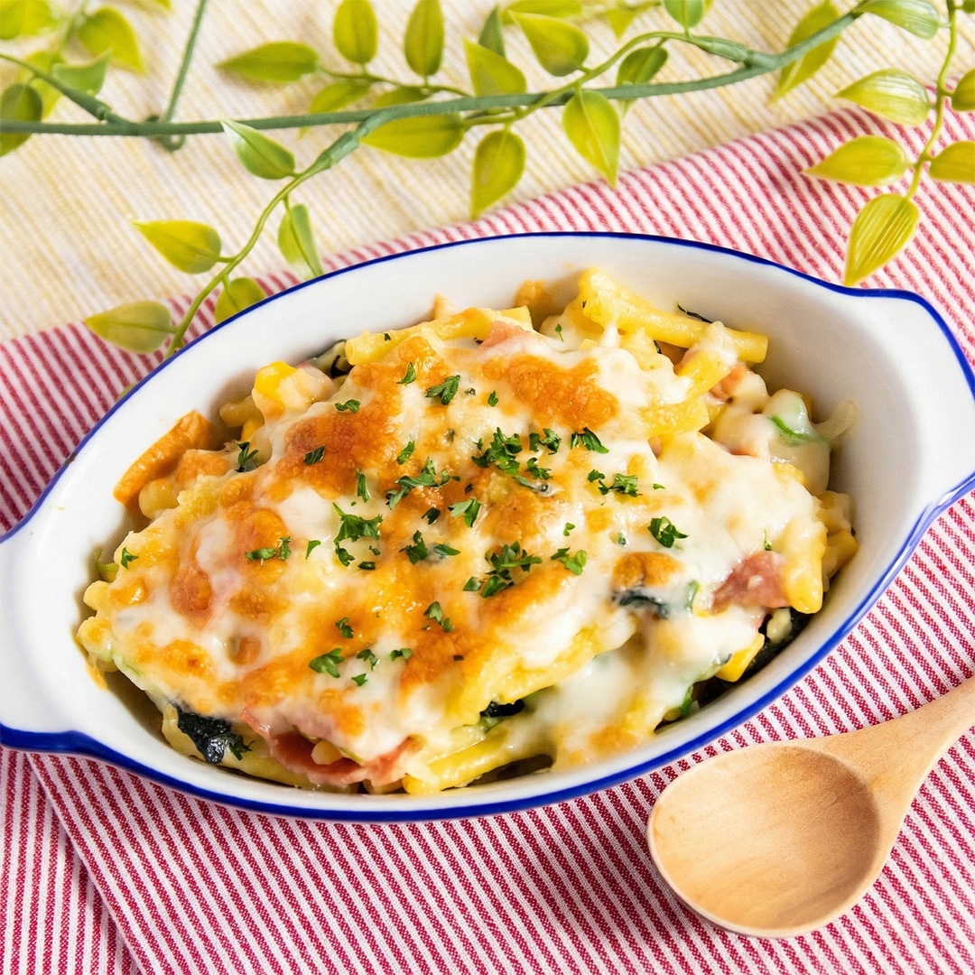 クリーミーなグラタンがオーブン皿に盛られ、木のスプーンがそばに置かれている。