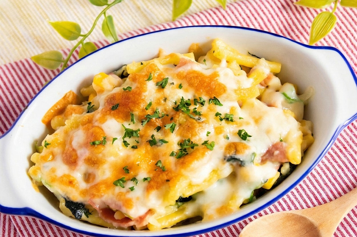 クリーミーなグラタンがオーブン皿に盛られ、木のスプーンがそばに置かれている。