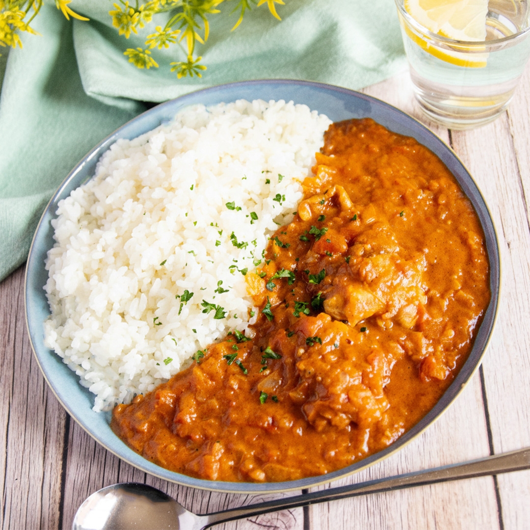ライスとカレーを盛り付けた皿。クロスと水のグラスが背景に配置されている。