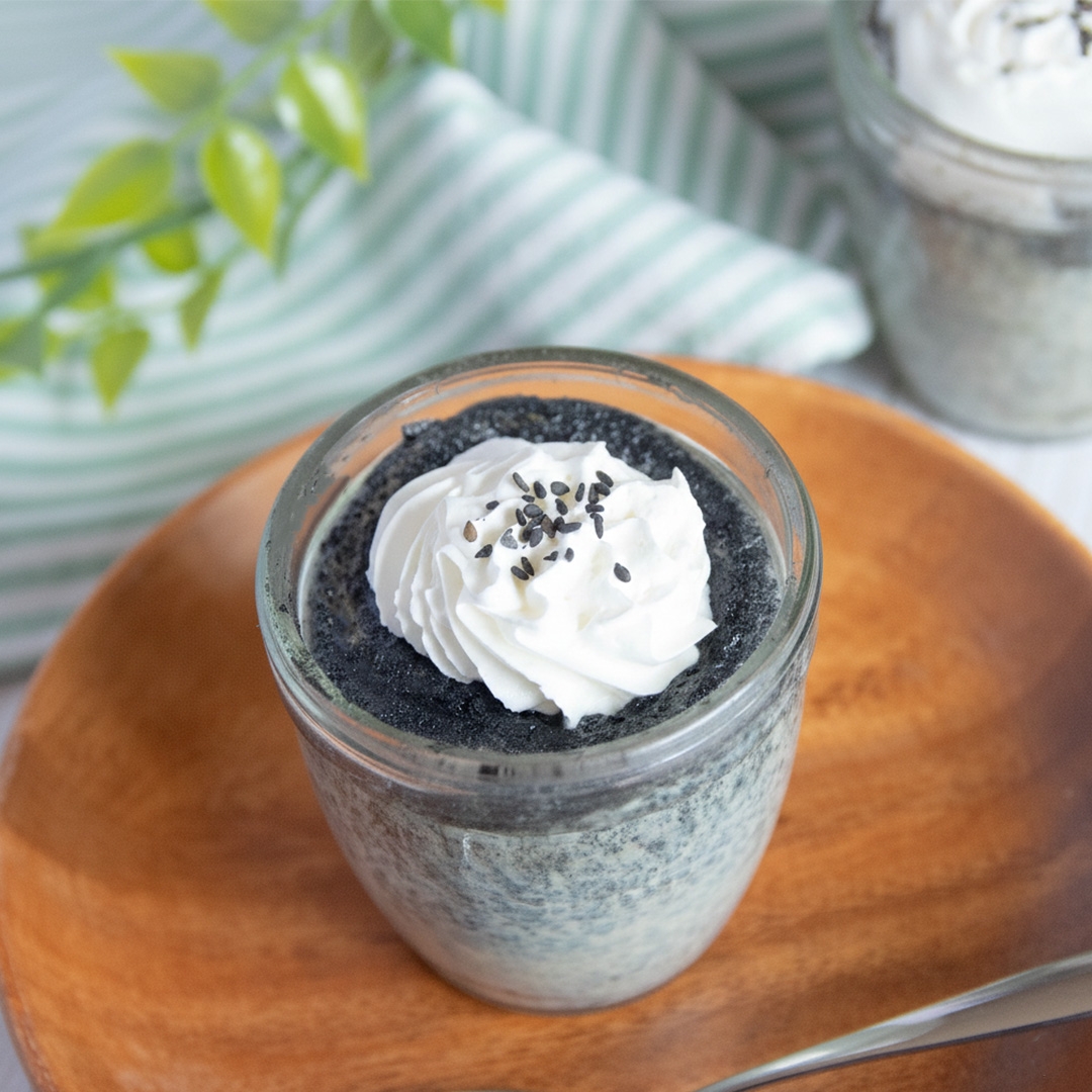 ガラスの容器に入った黒ごまプリン。ホイップクリームと黒ごまがトッピングされている。