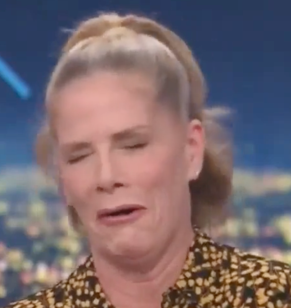 Person with a ponytail makes a humorous expression on a talk show set, wearing a patterned top