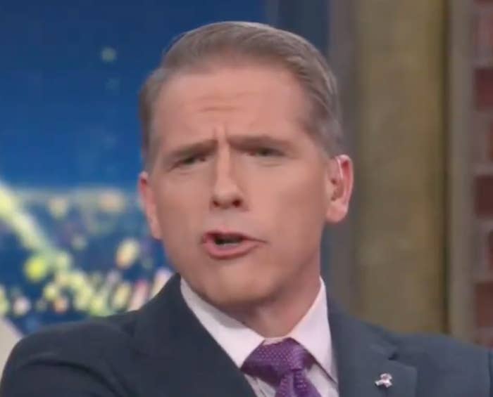 Person in a suit and tie speaking passionately on a talk show set