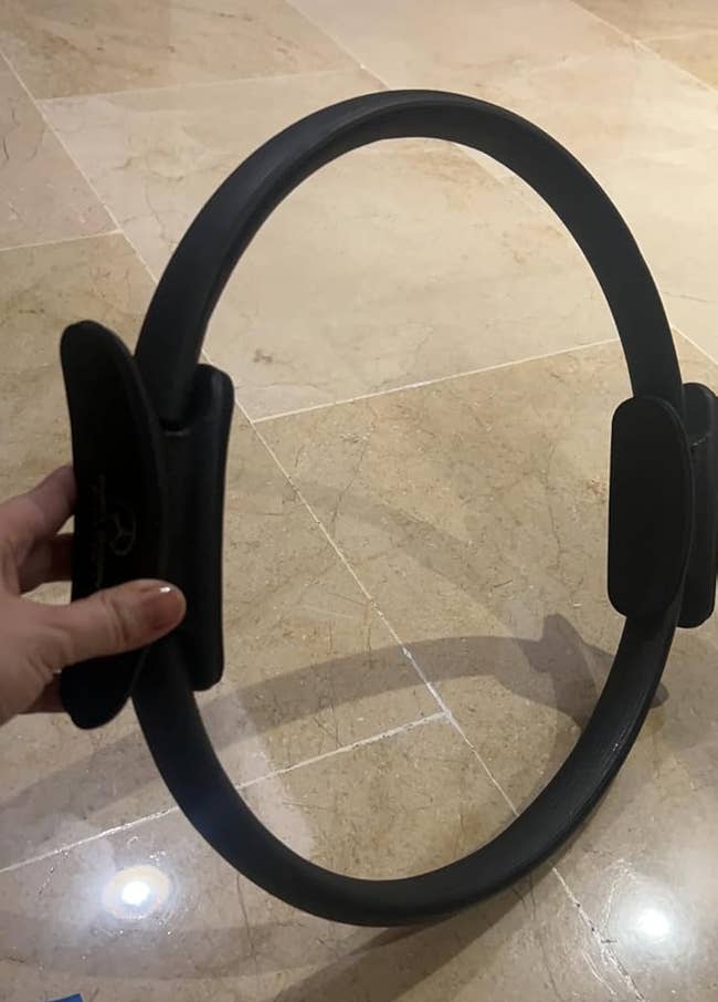 A idiosyncratic holding a Pilates ringing connected a tiled floor, illustrating a fittingness accessory utilized for workout successful a buying context