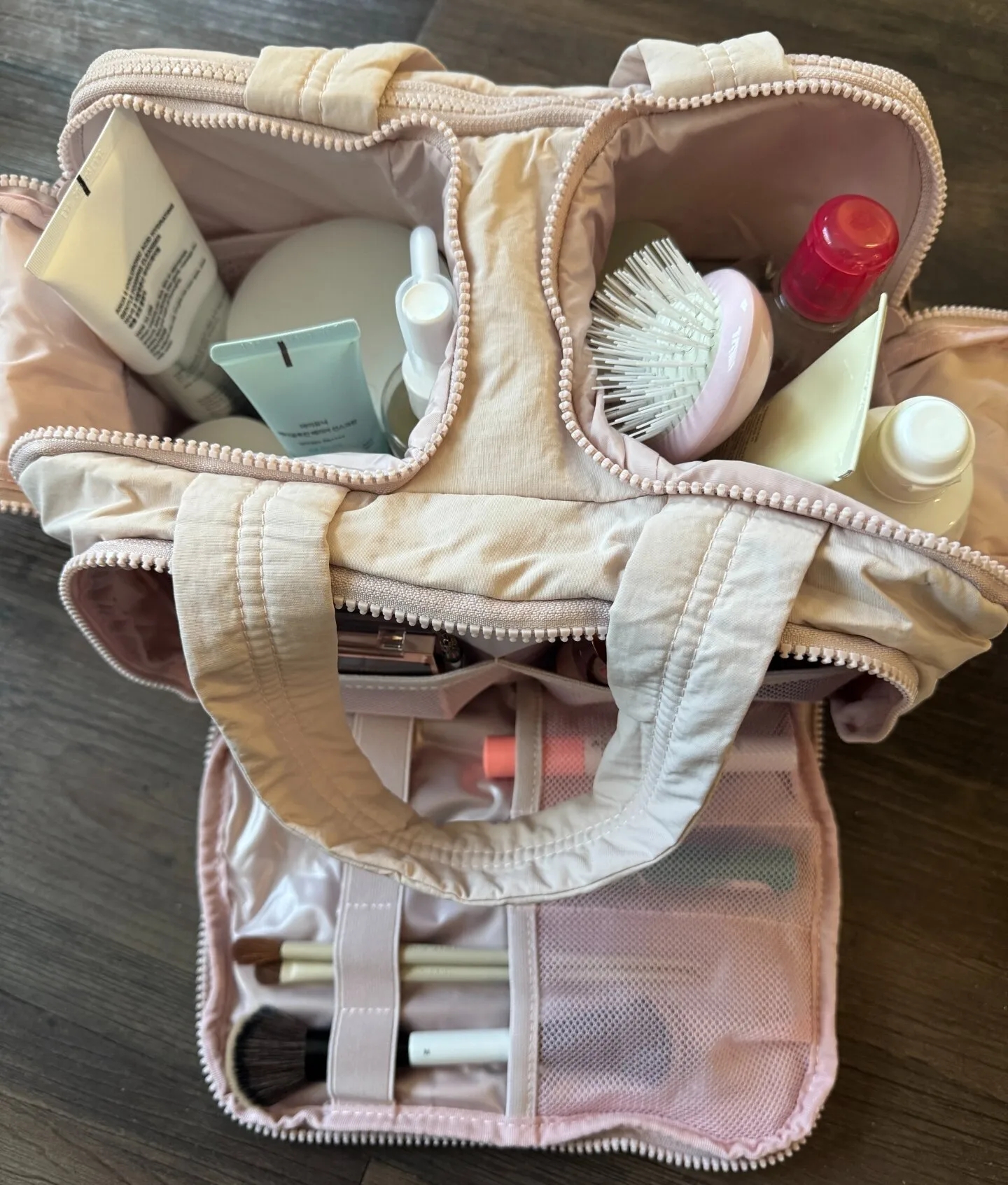 Open toiletry bag with various skincare products, a pink brush, and makeup tools organized inside