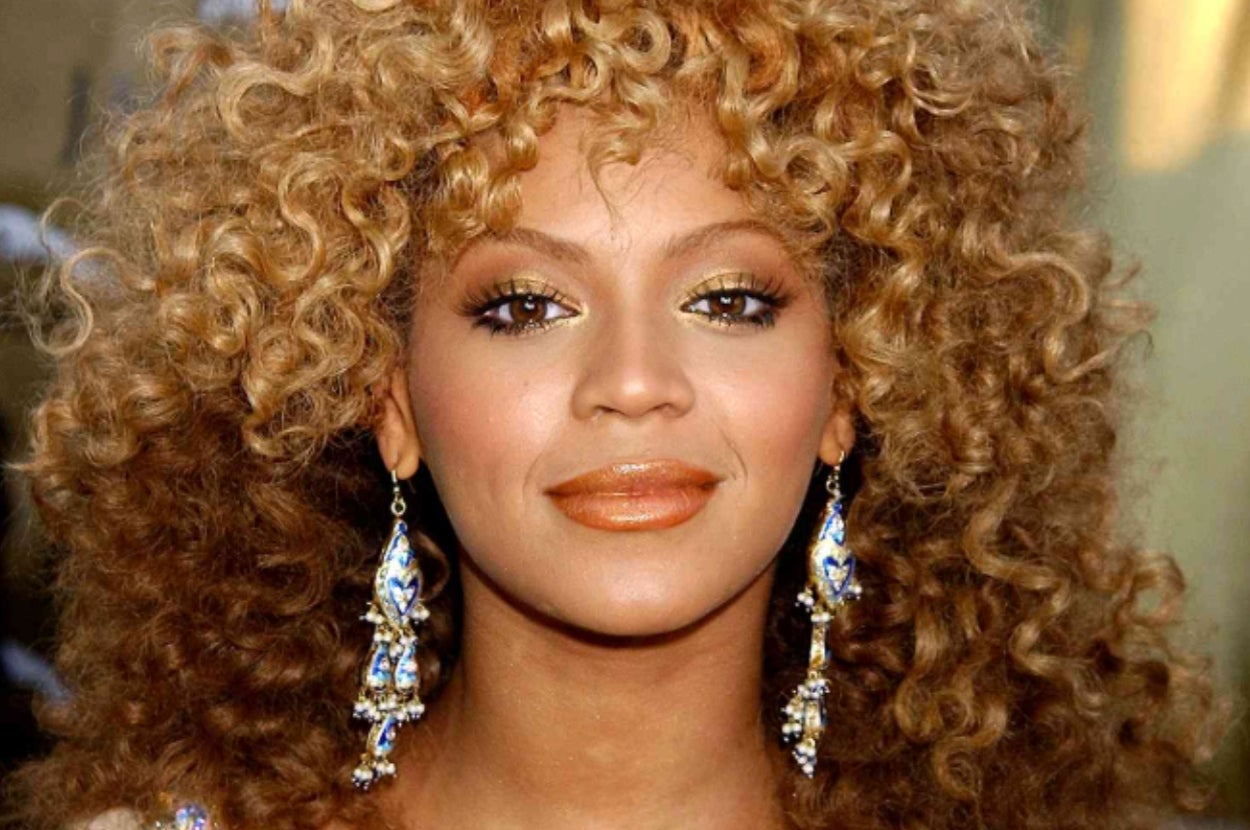 A person with curly hair wearing large, ornate earrings looks directly at the camera