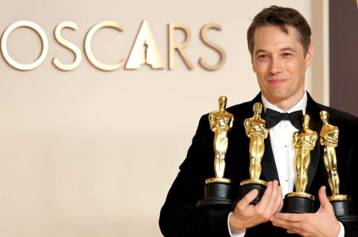 Person smiling in formal attire holding multiple awards at an event