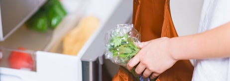 人がビニール袋に入った野菜を冷蔵庫から出し、エコバッグに入れている様子。