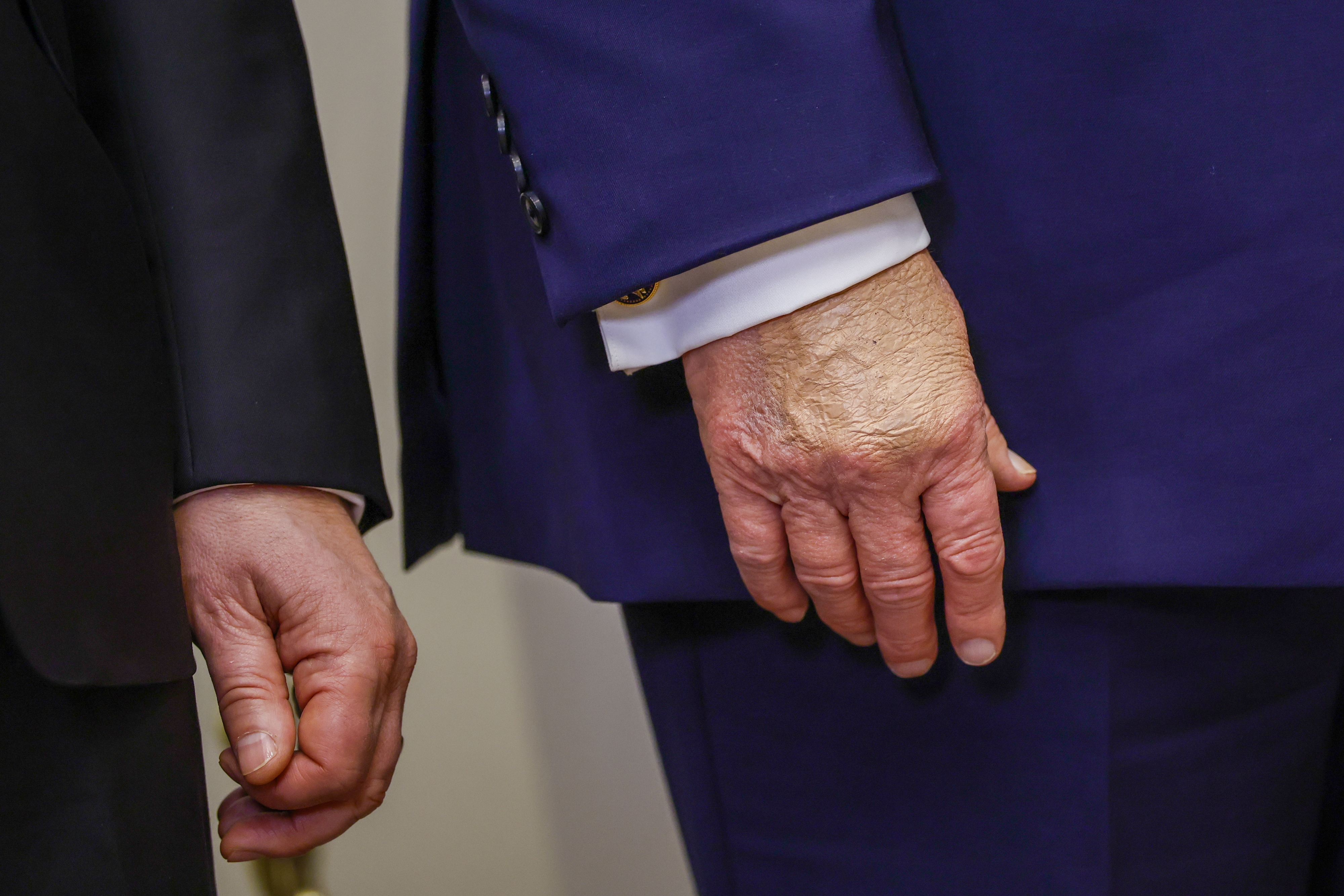 Two individuals in formal suits stand side by side, focusing on their hands and suit details