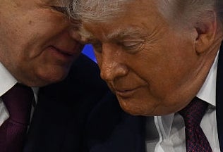 Two men in suits share a close conversation at a table with "Board of Peace" in the background