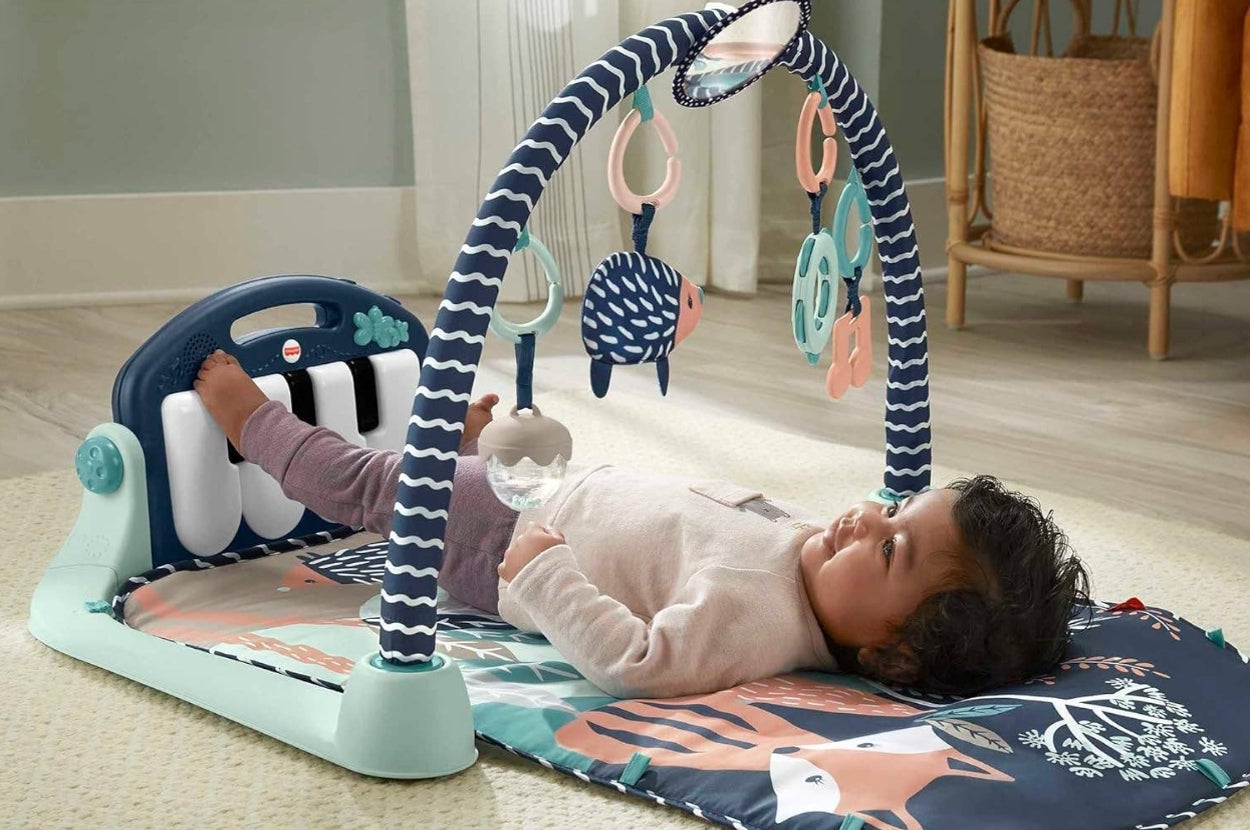 Baby lying on play mat with toy arch, featuring hanging toys and piano keys, indoors