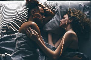 A couple lies in bed facing each other, gently embracing under soft lighting, symbolizing intimacy and connection