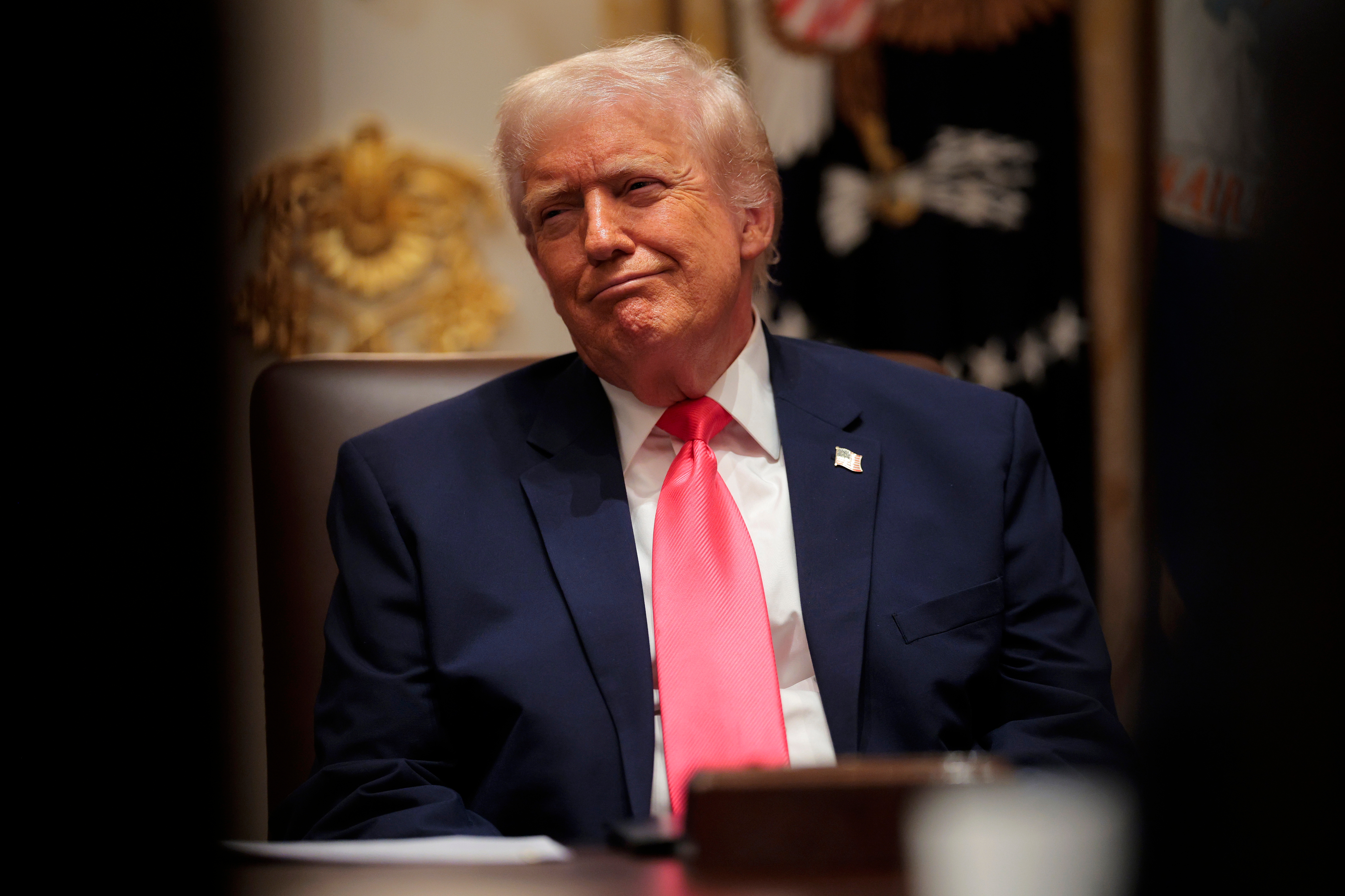 En person i dress med rødt slips sitter ved et bord og virker tankefull. Innstillingen foreslår et offisielt eller formelt miljø